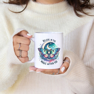 Person holding a mug with a butterfly design and text, wearing a white sweater.