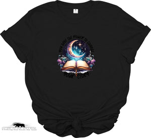 Black t-shirt with a colorful graphic design featuring a crescent moon, open book, and flowers on a white background.