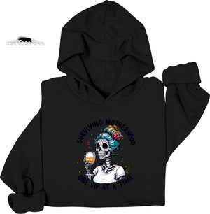 Black hoodie with a skeleton design holding a glass of wine and text 'Surviving Motherhood one sip at a time' on a white background.