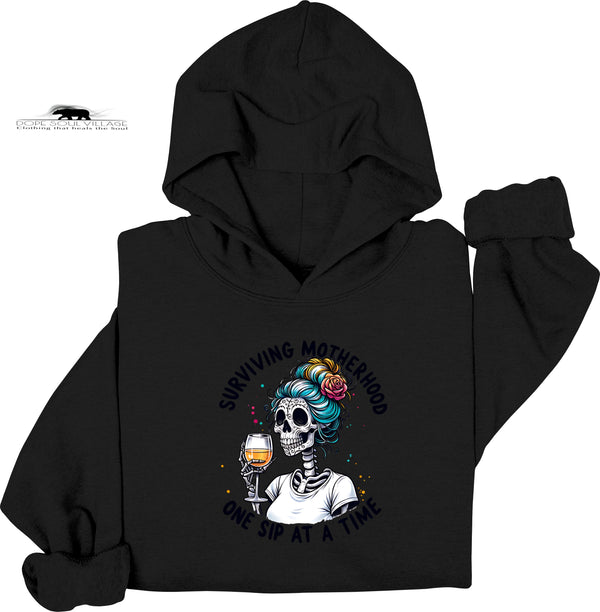 Black hoodie with a skeleton design holding a glass of wine and text 'Surviving Motherhood one sip at a time' on a white background.