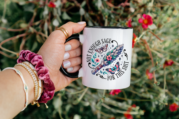 Hand holding a mug with floral design and text against a natural background