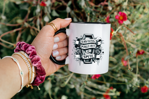 Hand holding a mug with a design and text, against a natural background with flowers.