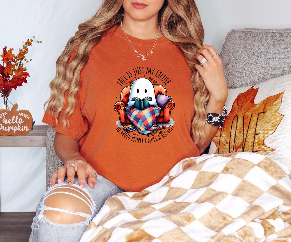 Person wearing an orange t-shirt with a graphic design, sitting on a couch with autumn decorations.