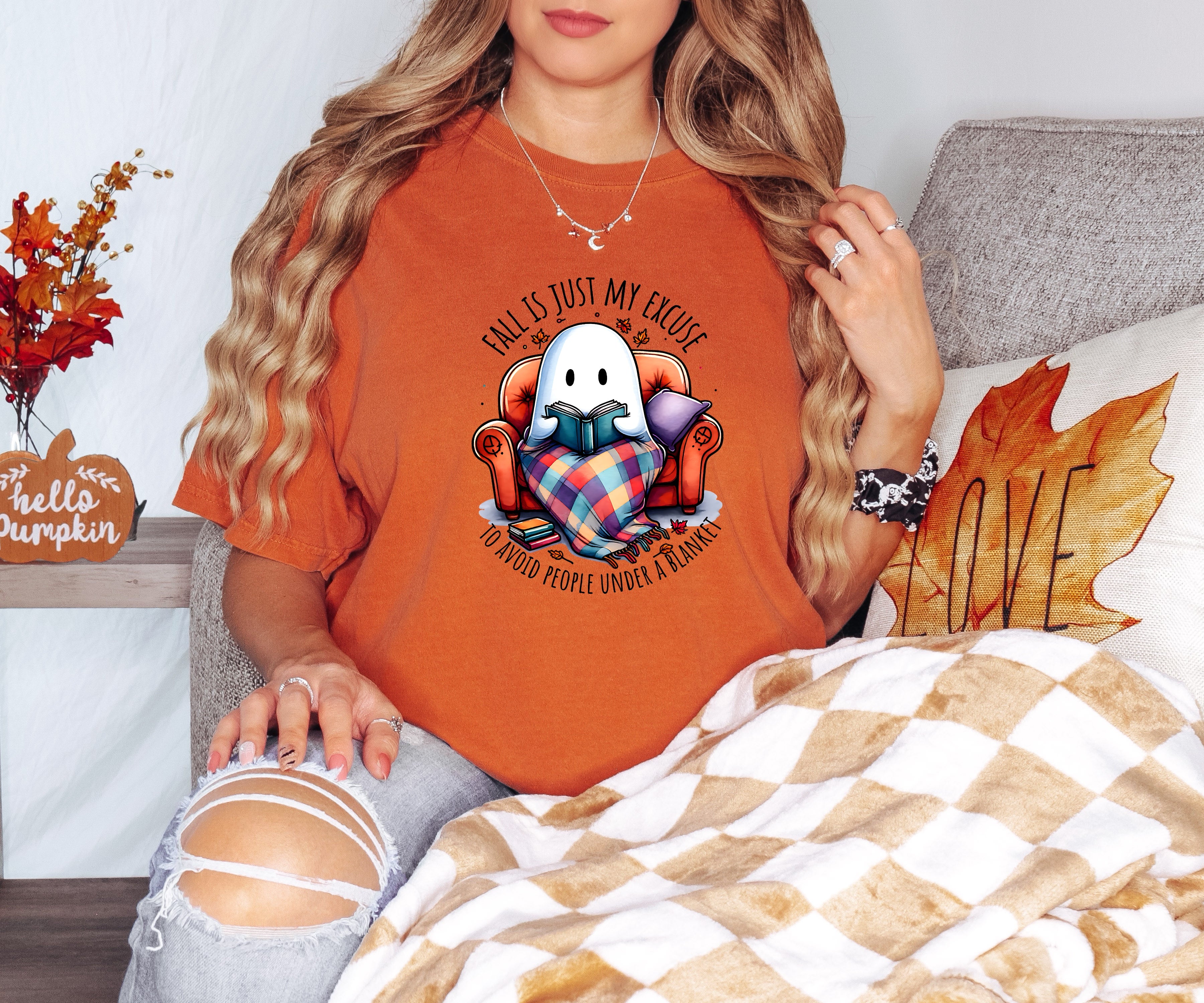 Person wearing an orange t-shirt with a graphic design, sitting on a couch with autumn decorations.