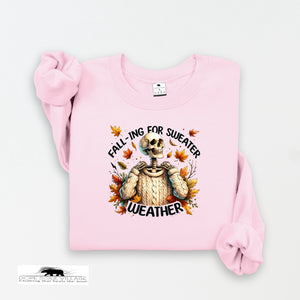 Pink sweatshirt with skeleton wearing a sweater graphic and text 'Falling for Sweater Weather' on a white background.