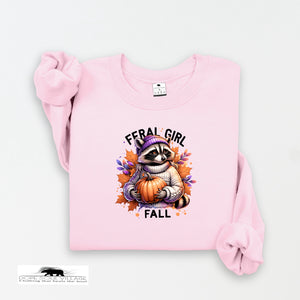 Pink sweatshirt with a raccoon holding a pumpkin and 'Feral Girl Fall' text on a white background
