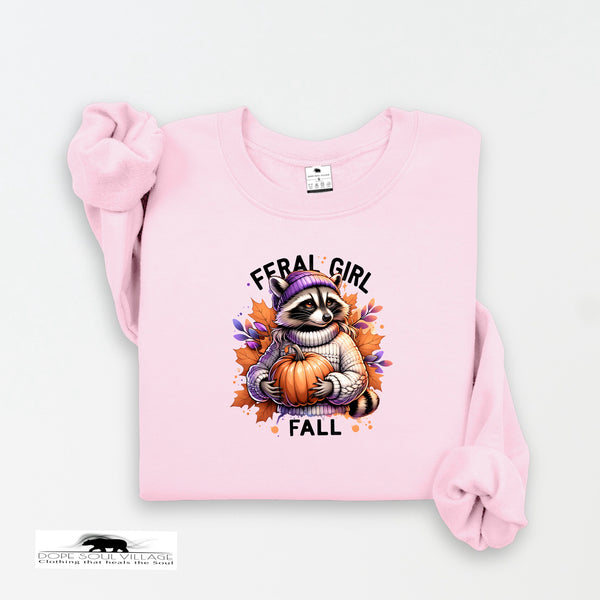 Pink sweatshirt with a raccoon holding a pumpkin and 'Feral Girl Fall' text on a white background