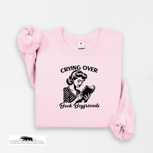 Pink sweatshirt with graphic and text 'Crying over Book Boyfriends' on a white background