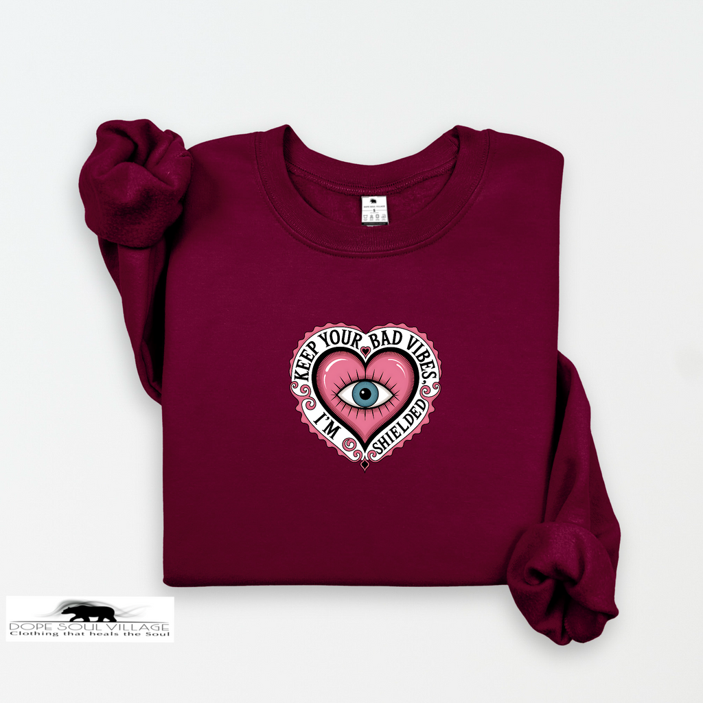 Maroon sweatshirt with a pink heart design featuring an eye and text on a white background.