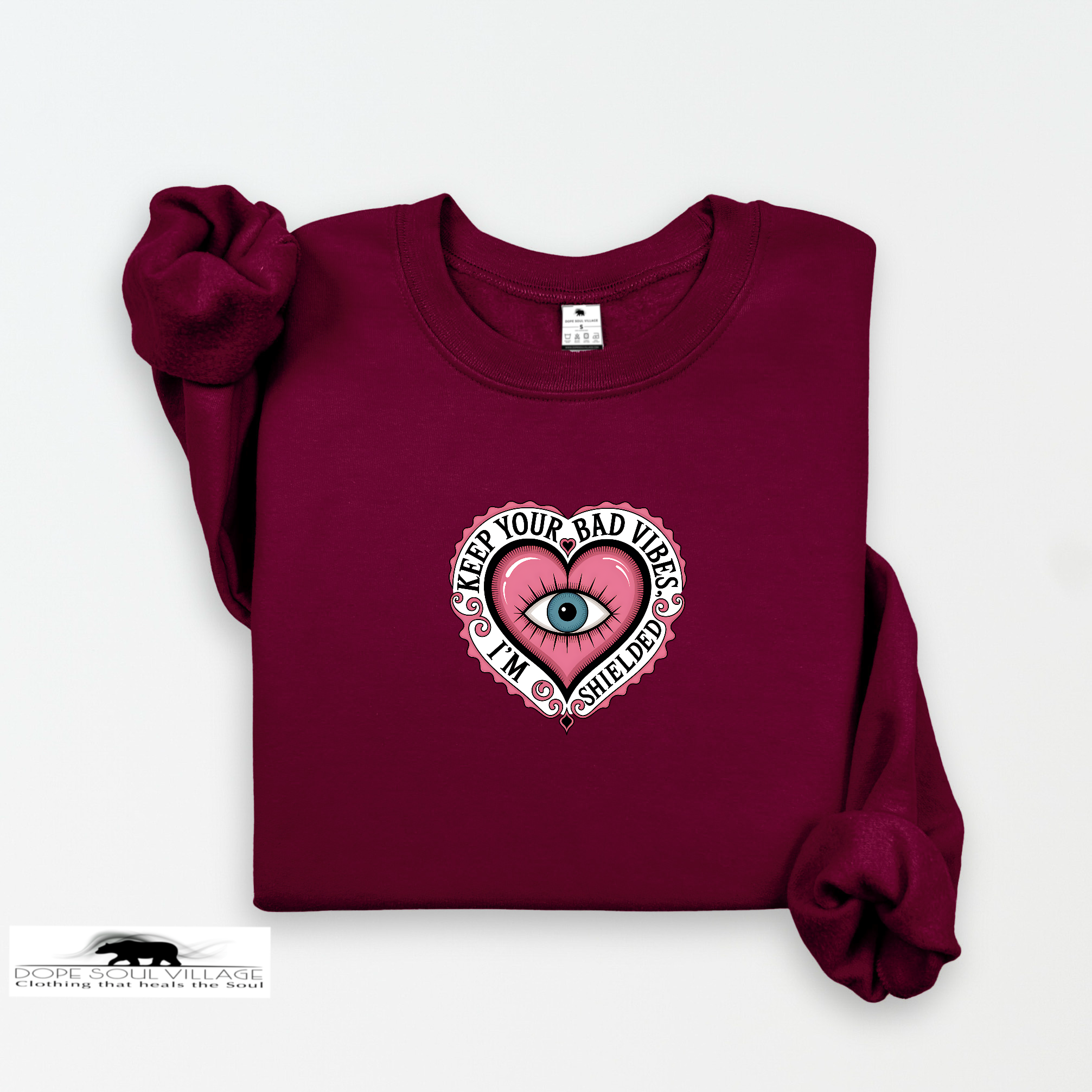 Maroon sweatshirt with a pink heart design featuring an eye and text on a white background.