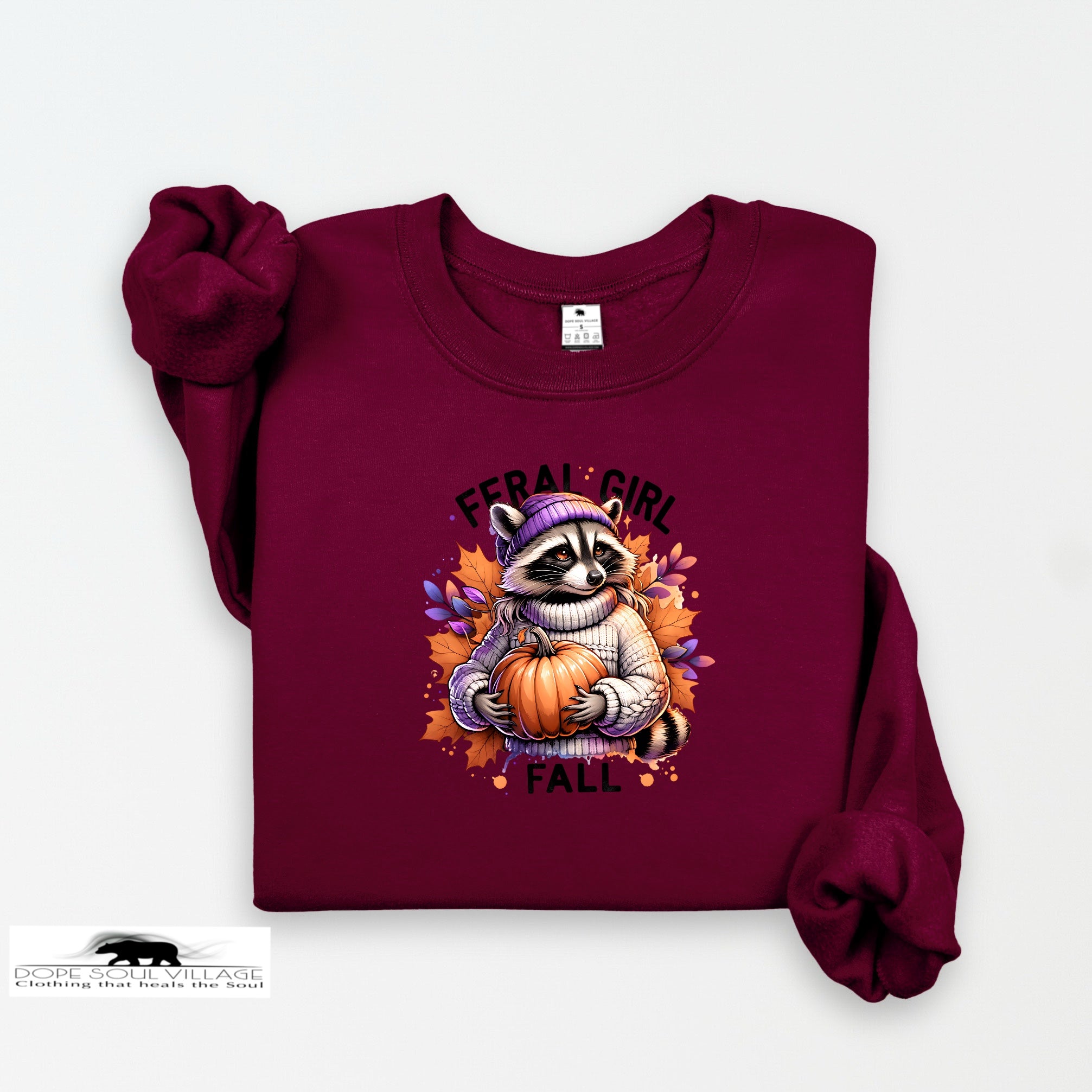 Maroon sweatshirt with a raccoon holding a pumpkin and 'Feral Girl Fall' text on a white background