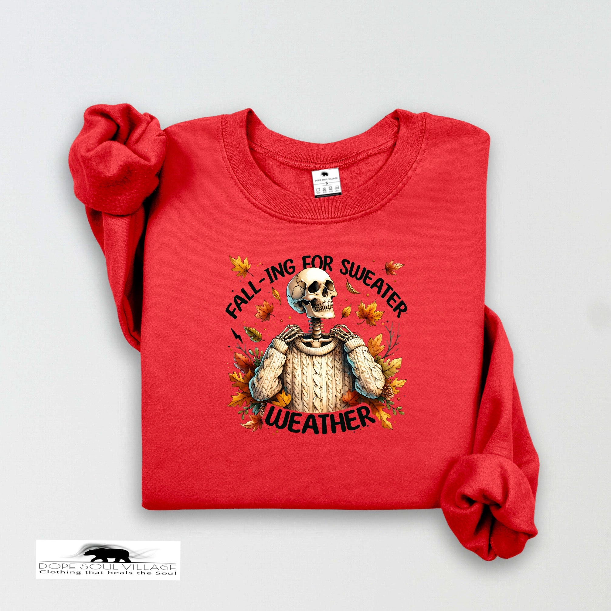 Red sweatshirt with skeleton design and text 'Fall-ing for Sweater Weather' on a light gray background.