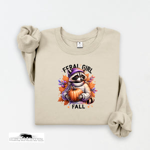 Beige sweatshirt with a raccoon holding a pumpkin and 'Feral Girl Fall' text on a white background