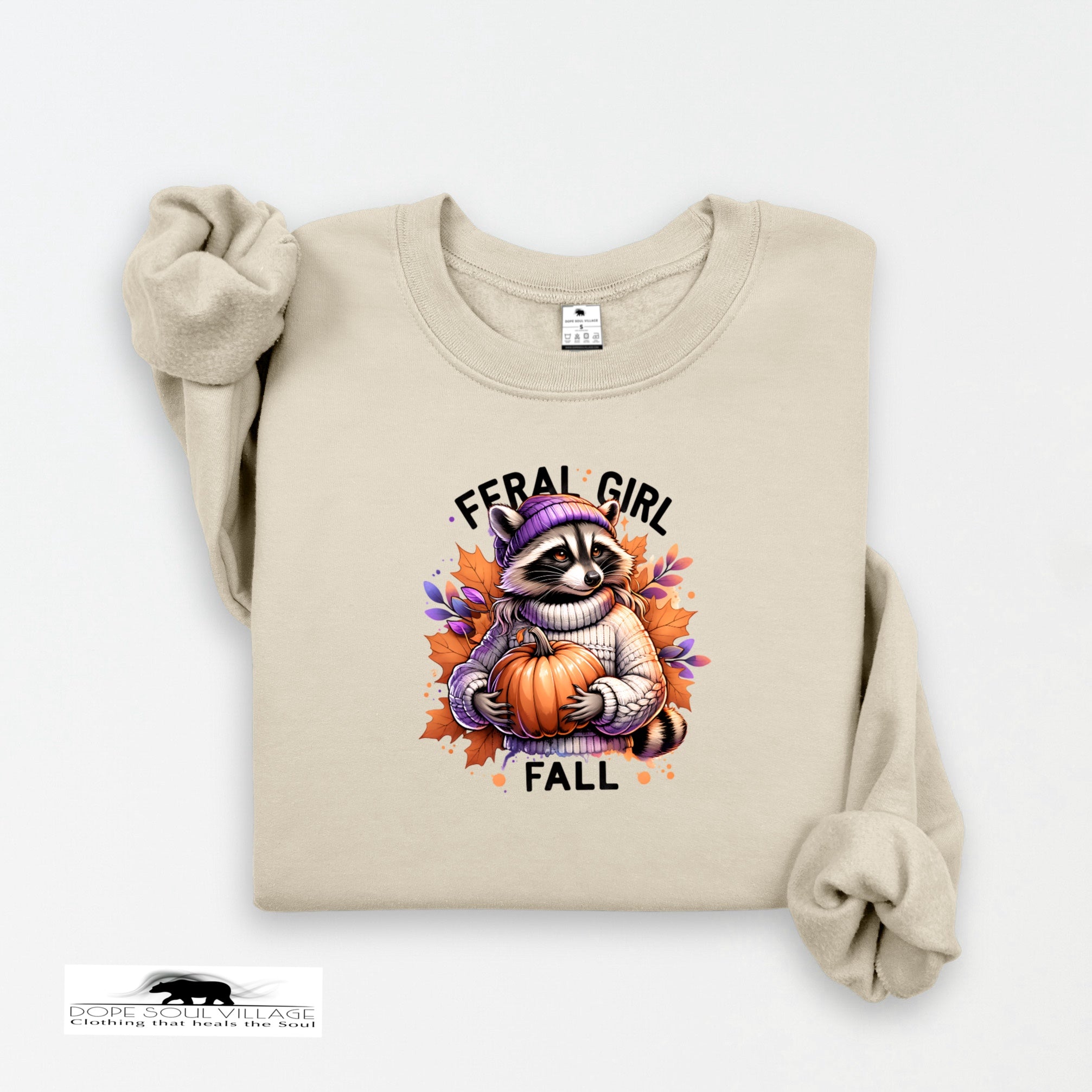 Beige sweatshirt with a raccoon holding a pumpkin and 'Feral Girl Fall' text on a white background