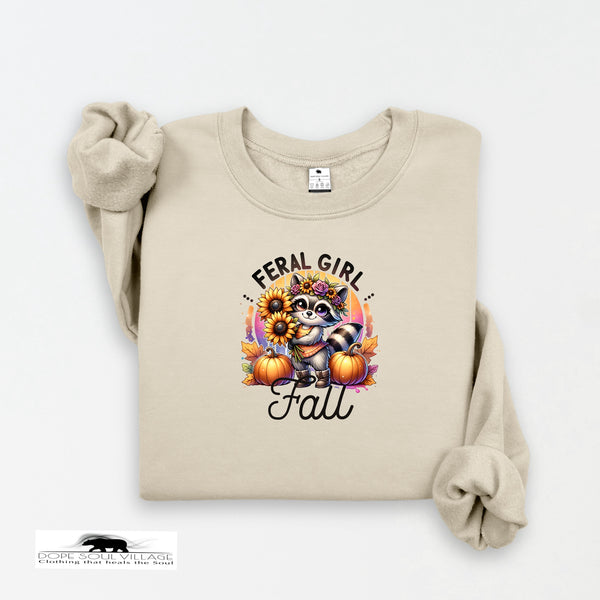 Beige sweatshirt with a raccoon graphic and 'Feral Girl Love Fall' text on a white background