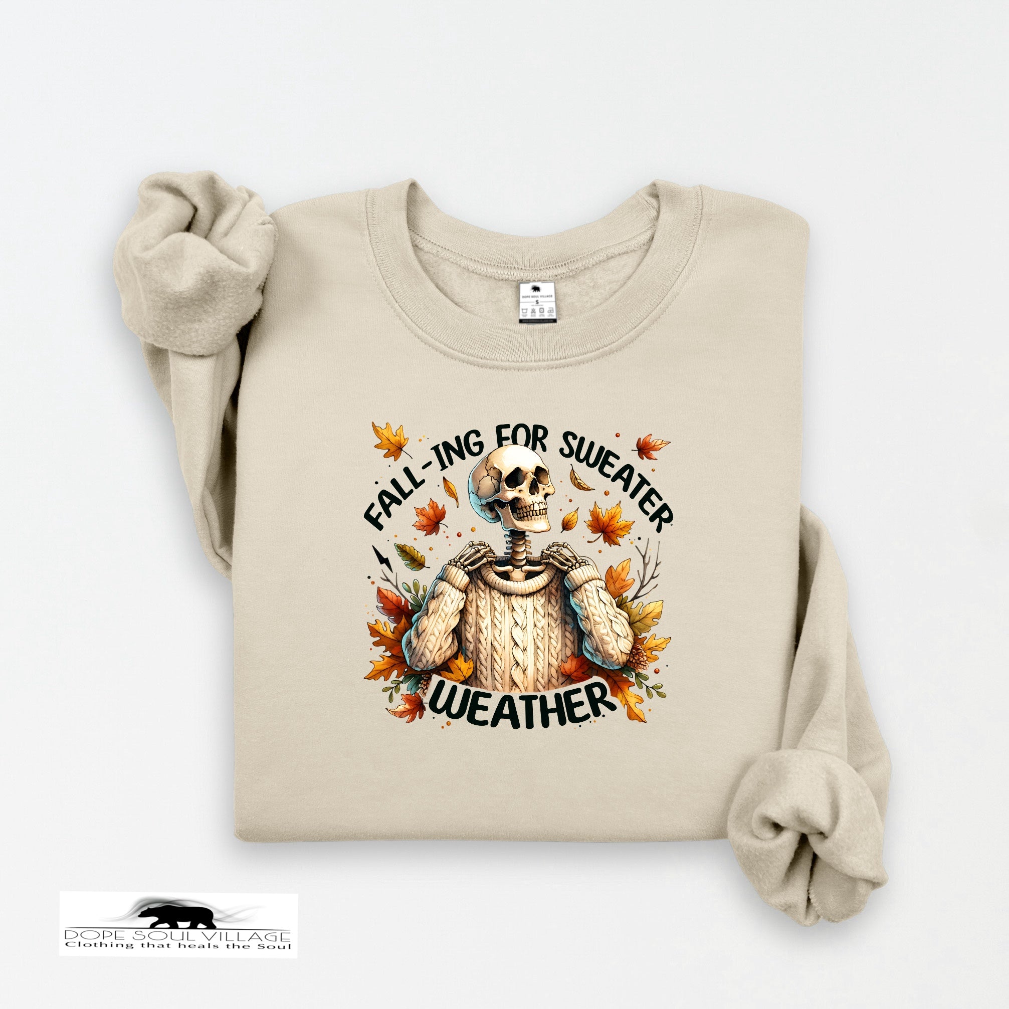 Beige sweatshirt with skeleton wearing a sweater and autumn leaves text on a white background