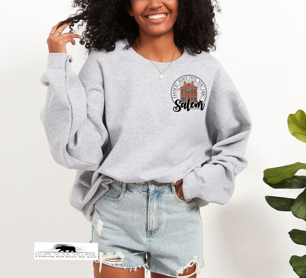 Woman wearing a gray sweatshirt with a logo and text, standing against a white background salem sister halloween collection dope soul village
