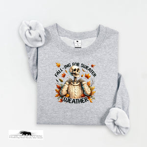 Gray sweatshirt with skeleton and 'fall-ing for sweater weather' text on a white background