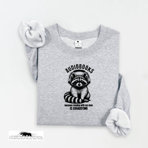 Gray sweatshirt with a raccoon wearing headphones and text 'AUDIODESks because reading with my eyes is exhausting' on a white background.