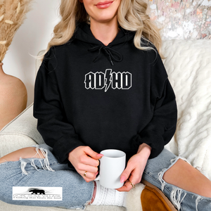 Person wearing a black hoodie with 'ADHD' text, holding a white mug, sitting on a couch.