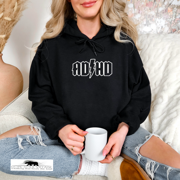 Person wearing a black hoodie with 'ADHD' text, holding a white mug, sitting on a couch.