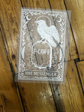 A clear vinyl decal sheet featuring a white engraved design of 'The Messenger' tarot card motif, including a bird, crescent moon, stars, and the text 'F-CAW-F', displayed on a rustic wooden plank floor.