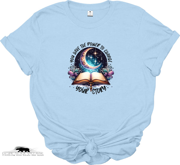 Light blue t-shirt with a graphic design of an open book, crescent moon, and stars on a white background.