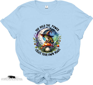 Light blue t-shirt with a witch and mushroom design and motivational text on a white background.