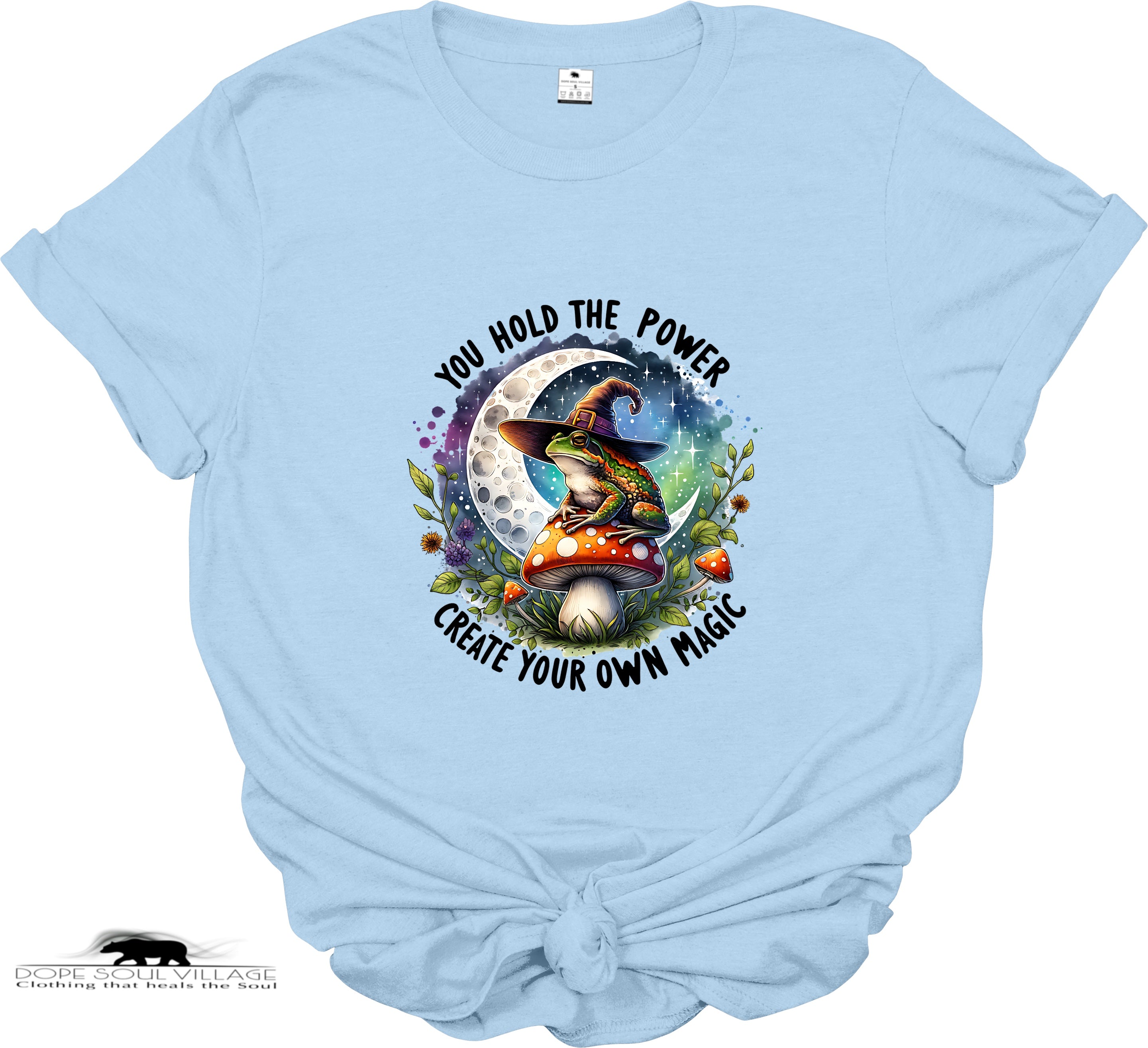 Light blue t-shirt with a witch and mushroom design and motivational text on a white background.