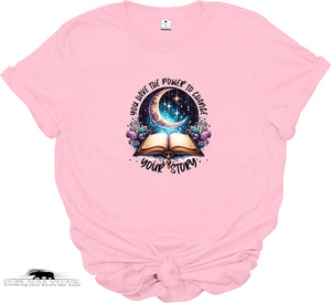 Pink t-shirt with a graphic design of an open book, crescent moon, and stars on a white background.