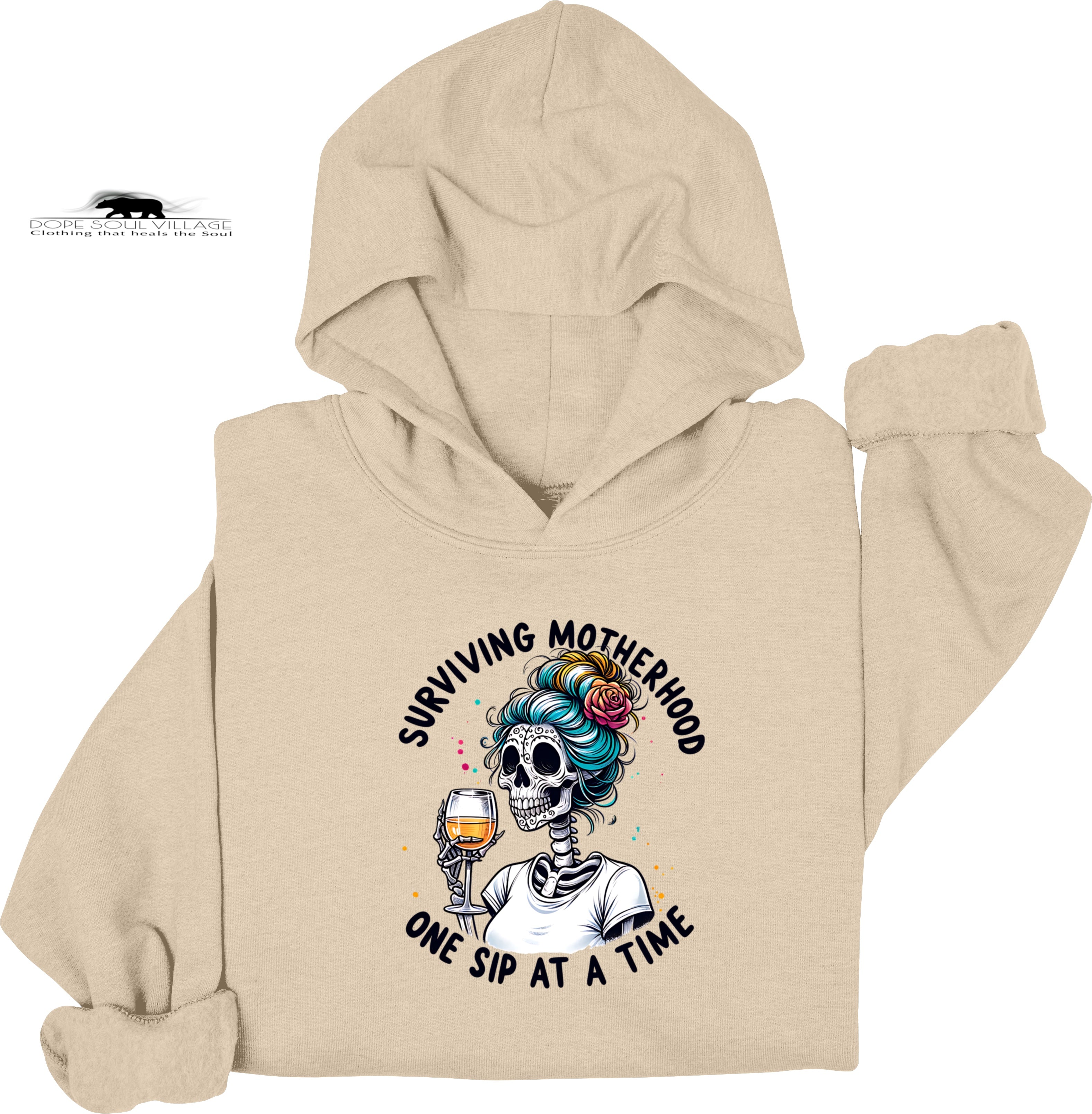 Beige hoodie with a graphic design of a skeleton with colorful hair and a glass of wine, text 'Surviving Motherhood One Sip at a Time', on a white background.