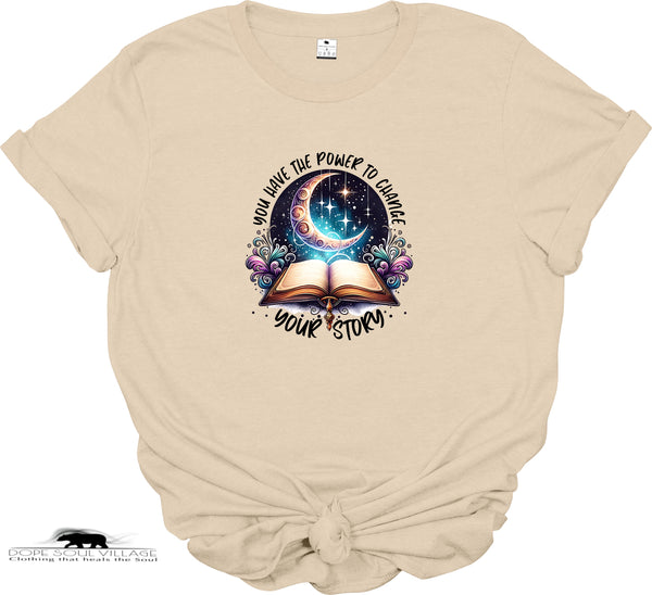 Beige t-shirt with a graphic design of an open book, moon, and stars with text on a white background.