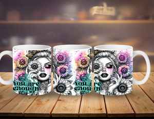 Three mugs with a design of a woman's face, flowers, and the text 'You are enough' on a wooden surface.