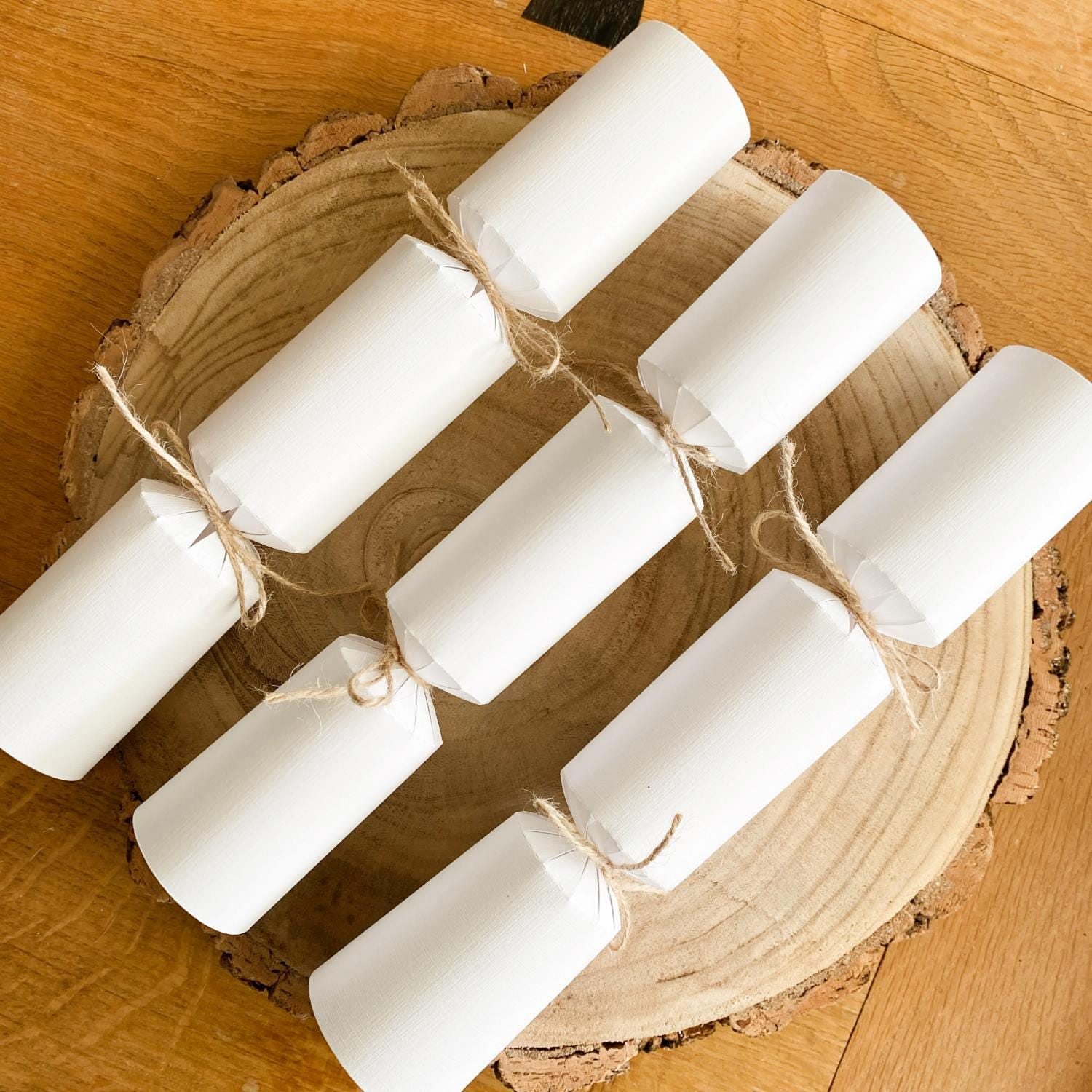 Three Christmas crackers from the white version of the DIY Christmas Cracker Kit resting on a wooden table