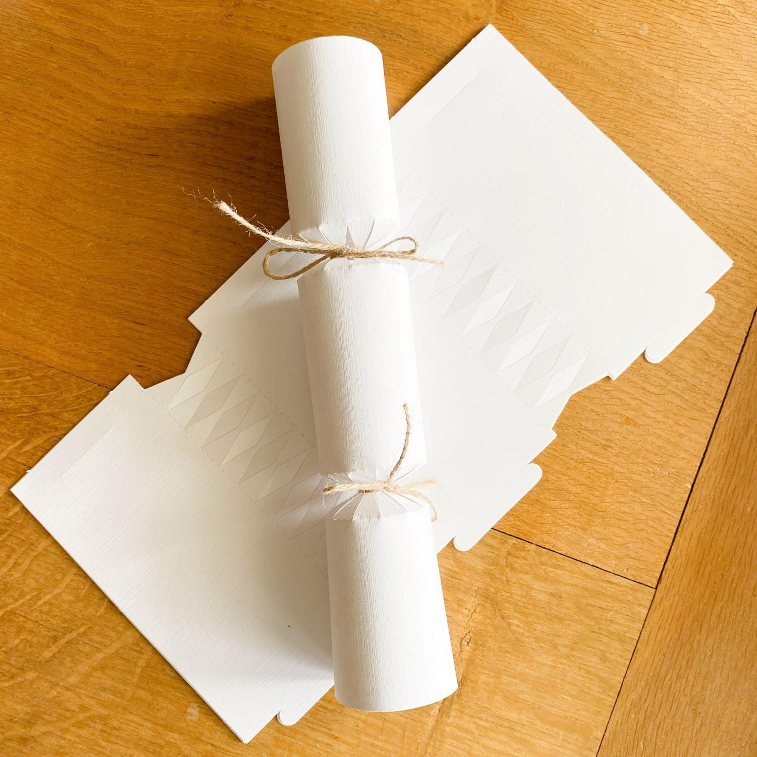 A white cracker blank from the DIY Eco-Friendly Christmas Cracker Kit, with a constructed white cracker lying across it.
