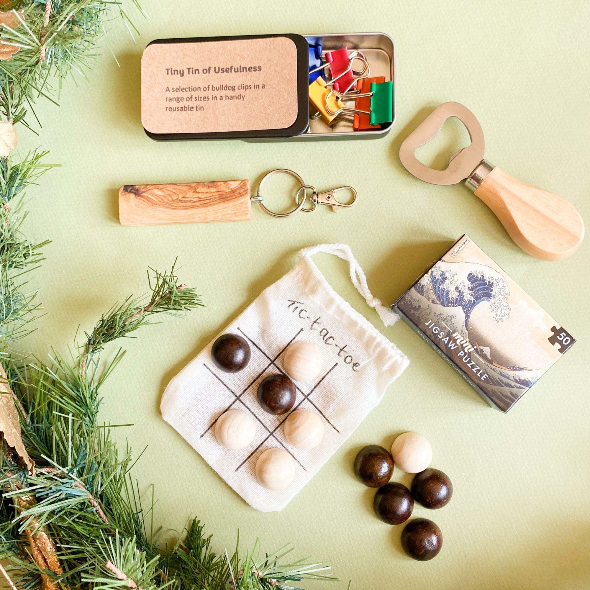 Close-up view of some of the eco-friendly cracker gifts, showing the wooden bottle opener, olive wood keyring, useful tin containing binder clips, wooden tic-tac-toe set and mini 50-piece jigsaw