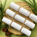 Homemade white Christmas crackers resting on a wooden board with green foliage around