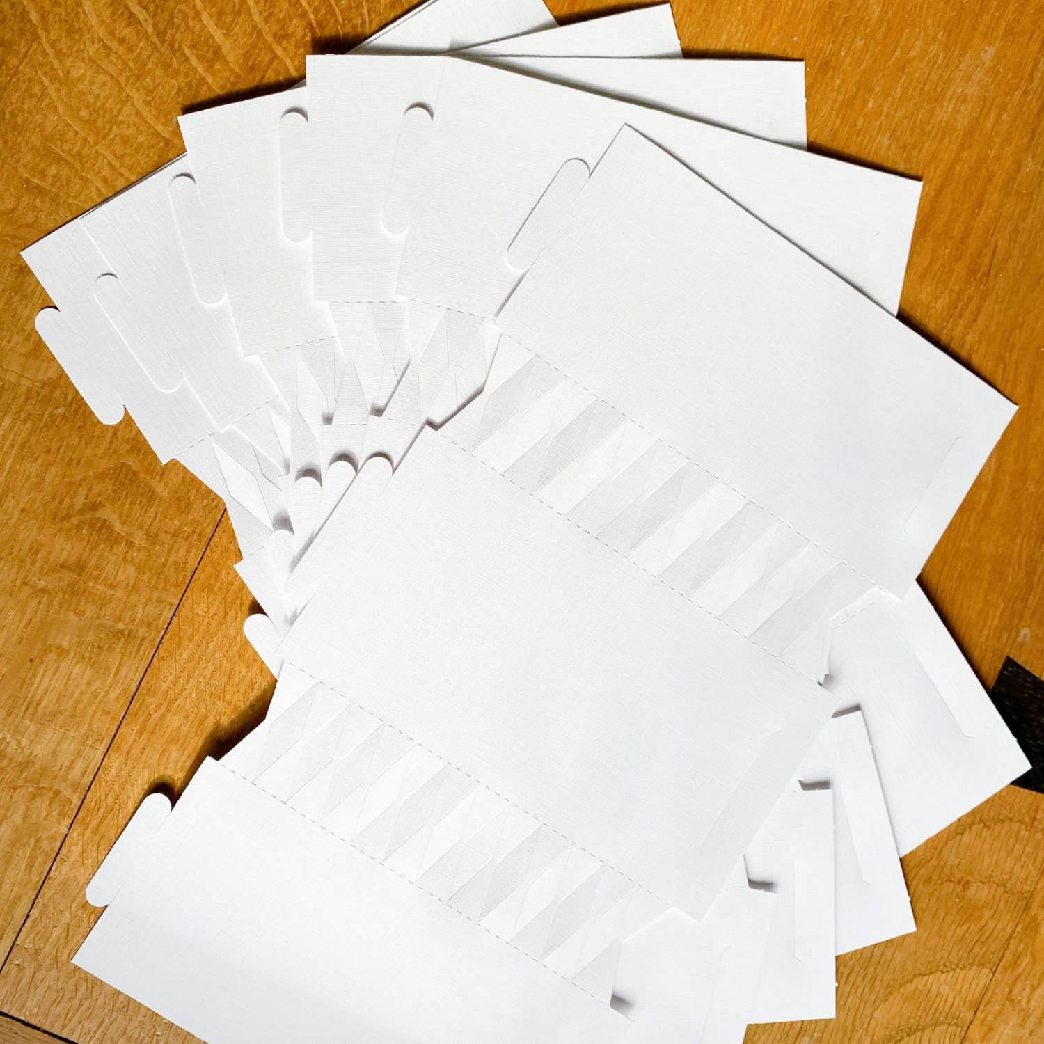 Six white cracker boards from the White DIY Christmas Cracker kit, fanned out on a wooden table.