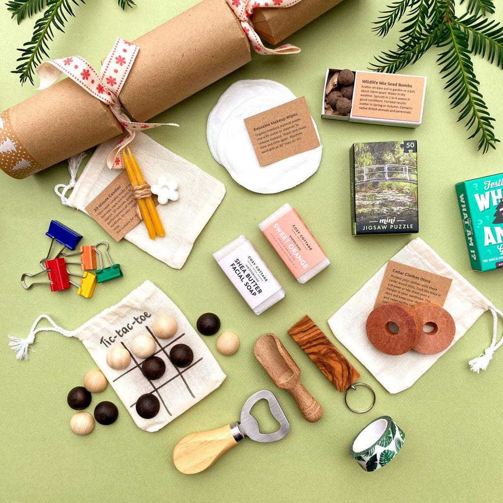 Selection of small, plastic-free gifts suitable for Christmas crackers, stocking fillers, Advent calendars or wedding favours, all arranged on a green background with the homemade Christmas cracker in the background.